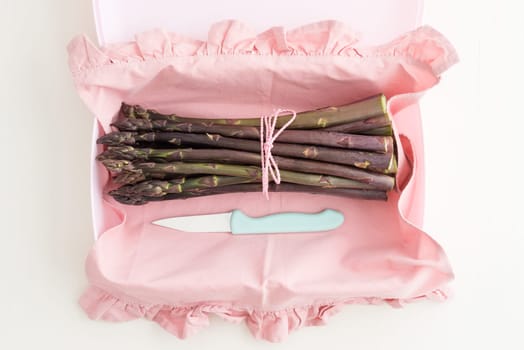 Bunch of purple asparagus in plastic tin with kitchen knife