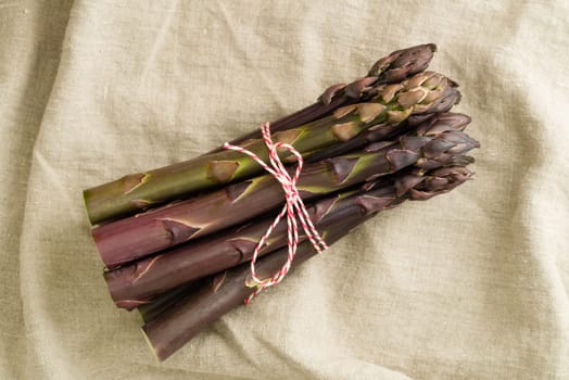 Bunch of violet asparagus on wooden table with linen cloth