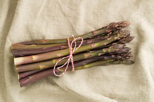 Bunch of violet asparagus on wooden table with linen cloth
