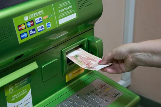 The hand of man (woman) insert a banknotes into a slot of the Sberbank ATM.