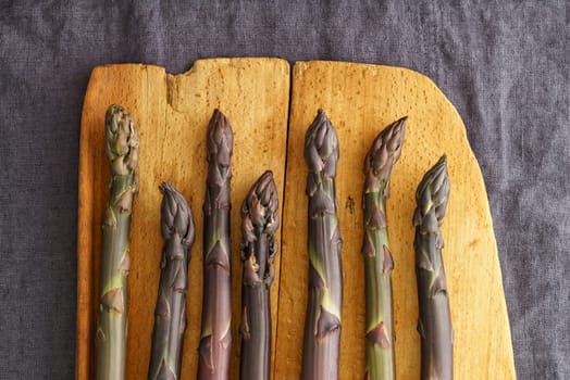 Fresh violet asparagus on an old wooden board on linen in a dark light mood