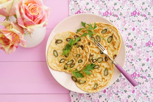 Pancakes with violet asparagus on pink plate with roses