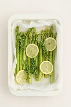Green asparagus with lemon slices for baking with baking paper in a baking dish