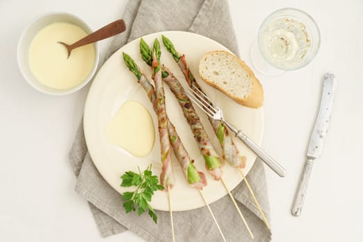 Bacon-wrapped grilled green asparagus skewers with Hollandaise sauce,baguette and white wine