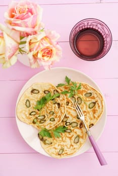 Pancakes with violet asparagus on pink plate with roses