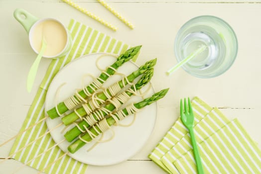 Steamed green asparagus on wooden skewers with spaghetti wrapped with hollandaise sauce