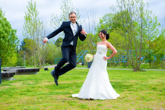 jumping bridegroom and his bride together in front of nature background