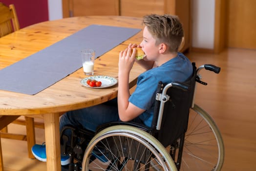 disabled boy in wheelchair is eating in the living room