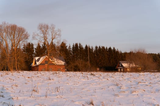 Winter forest and wooden houses in the evening in a snow-covered field, Kernave, Lithuania.