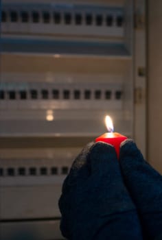Blackout, standing with a candle in front of a power fuse box, energy cut out, uncertain supply, risk and crisis for electricity