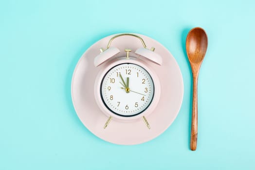 Alarm clock on a plate with a spoon in old retro style, pastel color, time to wake up in the morning, having lunch, taking a break