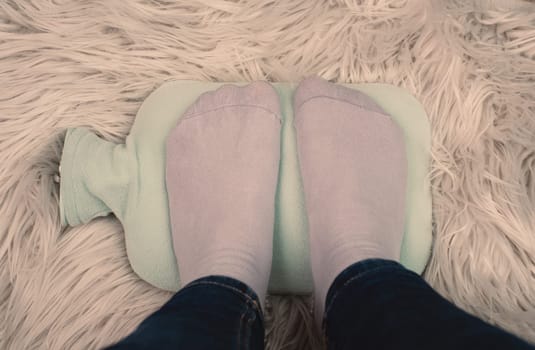 Warming the cold feet with a hot water bottle on a fur, freezing in winter, energy crisis