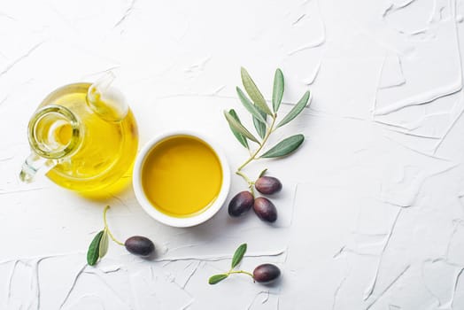 Olive oil in bowl with fresh olives fruit and olive branch on white background close up