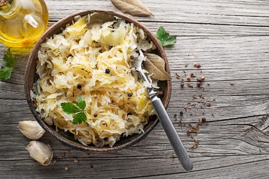 Homemade sauerkraut with black pepper and parsley in wooden bowl on rustic background. Top view. Copy space.