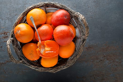 Ripe red and yellow orange persimmon fruit.Slices of persimmon. Close up of fresh kaki in basket on grey table.