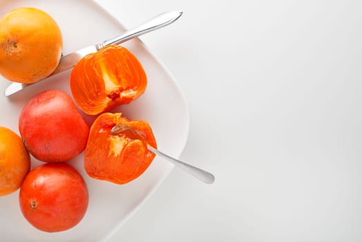Ripe red and yellow orange persimmon fruit.Slices of persimmon. Close up of fresh kaki on white table