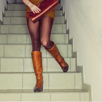 Cropped photo of female legs in brown tights and leather boots lifting dress