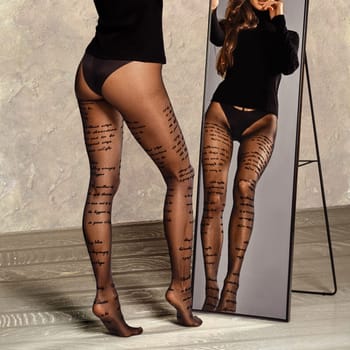 Beautiful female legs in pantyhose with inscriptions in front of the mirror