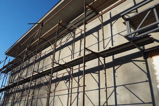 Scaffolding on a new one-story house. Facade works. Building bussiness. Low-rise private building. Plastering the wall of a building. Shop building. Metal production structures