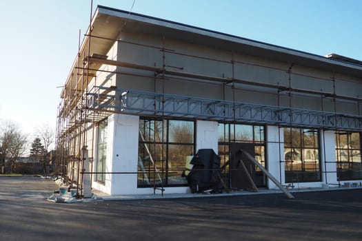 Scaffolding on a new one-story house. Facade works. Building bussiness. Low-rise private building. Plastering the wall of a building. Shop building. Metal production structures