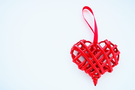 Red braided heart with a silk ribbon on a white background. Valentine's Day. copyspace. Nice souvenir - pendant