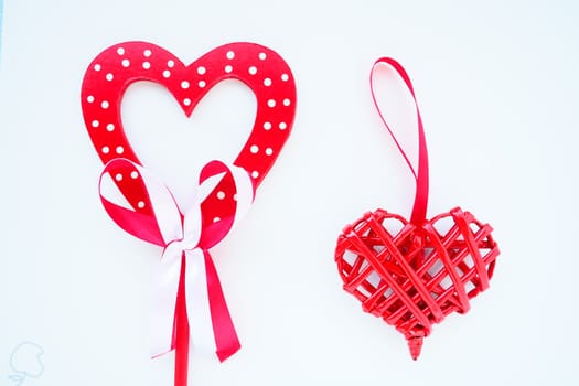 Valentine's day concept. Two red hearts. Wooden heart with white dots and a ribbon bow on a stick. Wicker heart with a loop. White background. Flat lay.