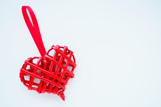 Red braided heart with a silk ribbon on a white background. Valentine's Day. copyspace. A nice souvenir - a pendant at an angle