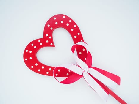 Valentine's day concept. Red wooden heart with white dots and ribbon bow on a stick. White background. A beautiful bow as a decoration. Love and relationships. Recognition or congratulations.