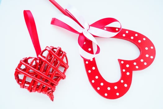 Valentine's day concept. Two red hearts. Wooden heart with white dots and a ribbon bow on a stick. Wicker heart with a loop. White background. Flat lay.