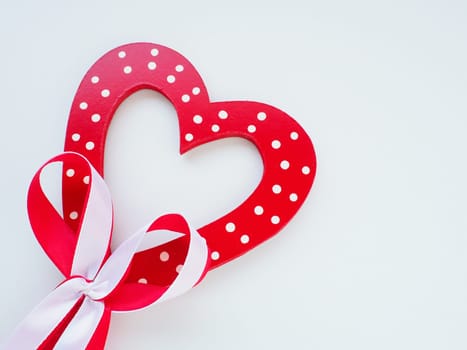 Valentine's day concept. Red wooden heart with white dots and ribbon bow on a stick. White background. A beautiful bow as a decoration. Love and relationships. Recognition or congratulations.