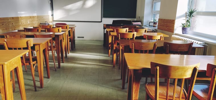 Music solfeggio empty class at school. The sun's rays fall on the floor through the window. Wooden student tables and chairs. School board and white walls. School interior