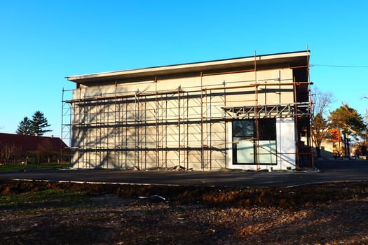 Scaffolding on a new one-story house. Facade works. Building bussiness. Low-rise private building. Plastering the wall of a building. Shop building. Metal production structures