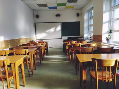 Music solfeggio empty class at school. The sun's rays fall on the floor through the window. Wooden student tables and chairs. School board and white walls. School interior