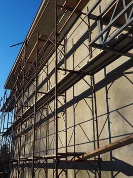 Scaffolding on a new one-story house. Facade works. Building bussiness. Low-rise private building. Plastering the wall of a building. Shop building. Metal production structures