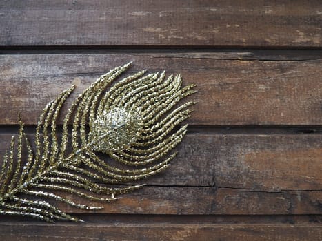 Golden peacock feather. Decorative gilded branch in the shape of a peacock's tail and eyelet. Wooden background. Festive decoration and beautiful carnival decor. Flat lay copy space.