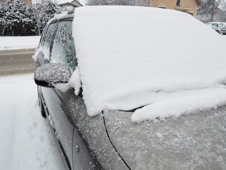 Snow and ice on the windshield, retrovisors and rear-view mirrors of the car. Winter driving conditions. Snow cleaning. Road traffic in winter. Metallic car. Snowdrifts and slush