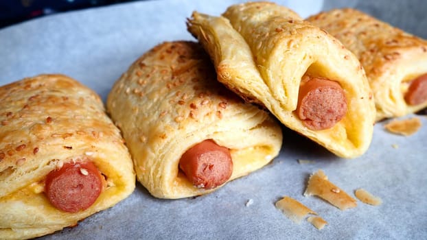 Sausages in the dough on a baking sheet with baking paper. Delicious fresh pies from the oven. Yeast dough culinary products with milk sausages. Sprinkling with sesame seeds.