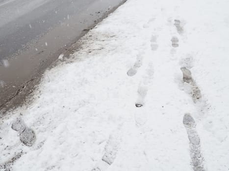 Roadside with a snowdrift. Difficult driving conditions. Wet slippery pavement with footprints. Dangerous ice. Muddy weather in winter. Car tire tracks. The work of municipal services for cleaning.