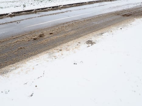 Roadside with a snowdrift. Difficult driving conditions. Wet slippery pavement with footprints. Dangerous ice. Muddy weather in winter. Car tire tracks. The work of municipal services for cleaning.