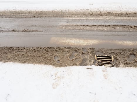 Snow, ice, slush and winter mud at a pedestrian crossing. The air temperature is about 0. Difficult driving conditions. Braking distance of the car. Underground drain with metal grate. Snow melting.