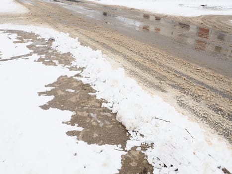 Roadside with a snowdrift. Difficult driving conditions. Wet slippery pavement with footprints. Dangerous ice. Muddy weather in winter. Car tire tracks. The work of municipal services for cleaning.