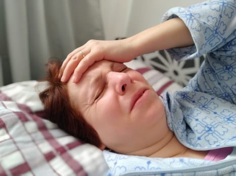 Sick woman in bed. Headache, runny nose and cold. Paleness of the face and faintness of the body. Feeling unwell. The patient lies on a pillow, holding forehead with his hand. Sharp pain and grimace.