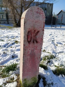 Strange concrete pillar in the city. Pink monument on the grave with the inscription OK. City engineering communications and designations. Snow with footprints