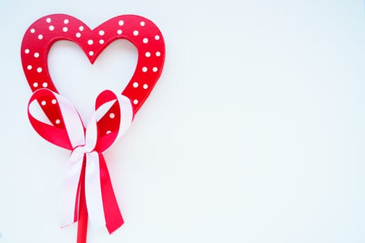 Valentine's day concept. Red wooden heart with white dots and ribbon bow on a stick. White background. A beautiful bow as a decoration. Love and relationships. Recognition or congratulations.