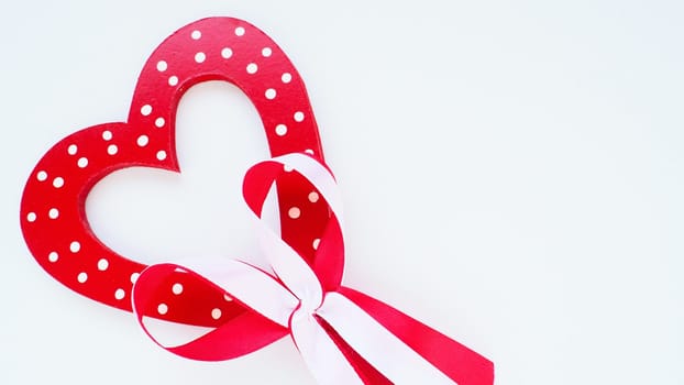 Valentine's day concept. Red wooden heart with white dots and ribbon bow on a stick. White background. A beautiful bow as a decoration. Love and relationships. Recognition or congratulations.