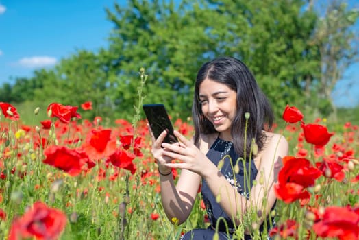 young woman with smartphone in poppy field