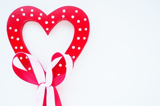 Valentine's day concept. Red wooden heart with white dots and ribbon bow on a stick. White background. A beautiful bow as a decoration. Love and relationships. Recognition or congratulations.