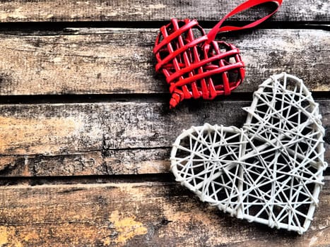 A wicker hearts a wooden background. Two red braided heart with hanging loop. White big heart. Two lovers. Valentine's Day Theme. Horizontal boards. copyspace. Flat lay.