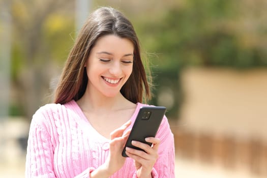 Happy teen in pink using phone walking in the street