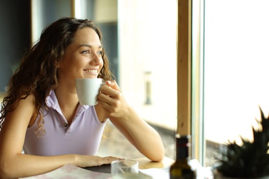 Happy woman holding coffee cup in a restaurant looks away through a window